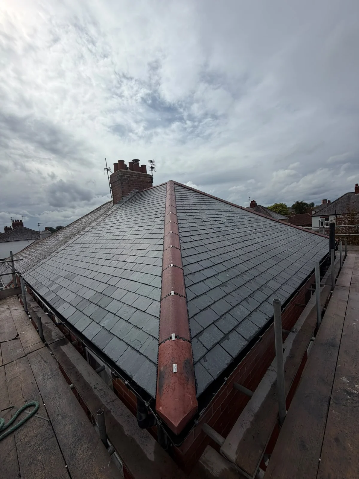 Natural slate hip roof with red ridge tiles and a brick chimney