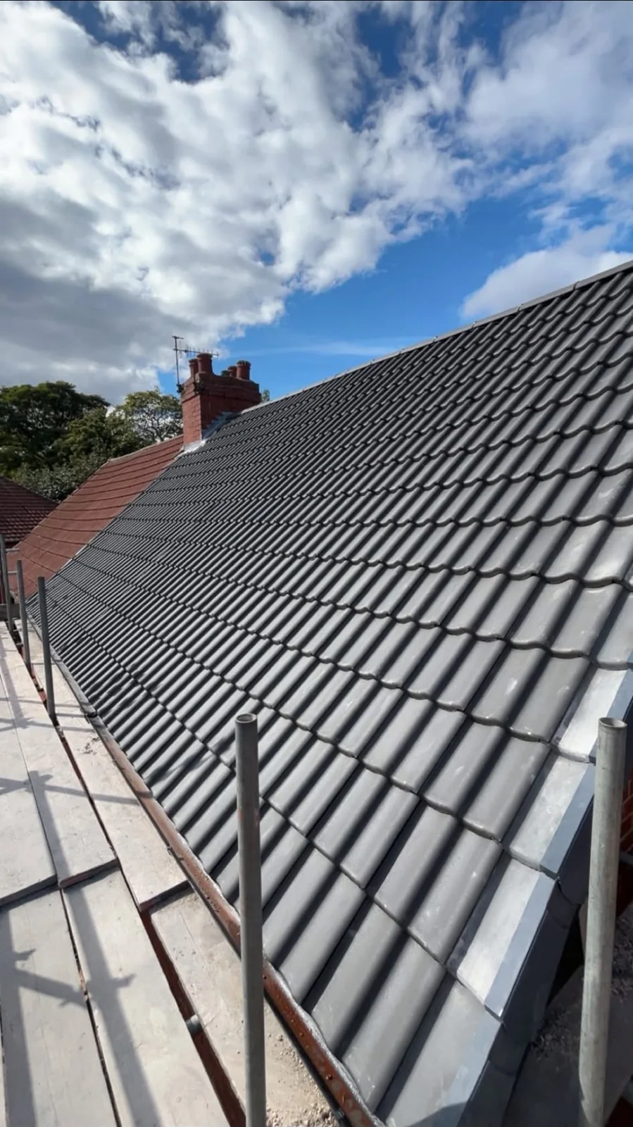 New grey double roman tiled roof beside a brick chimney